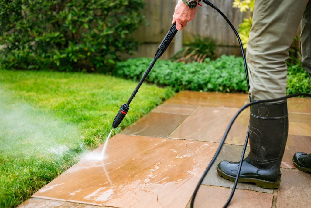 Senior man cleaning patio tiles using pressure washer